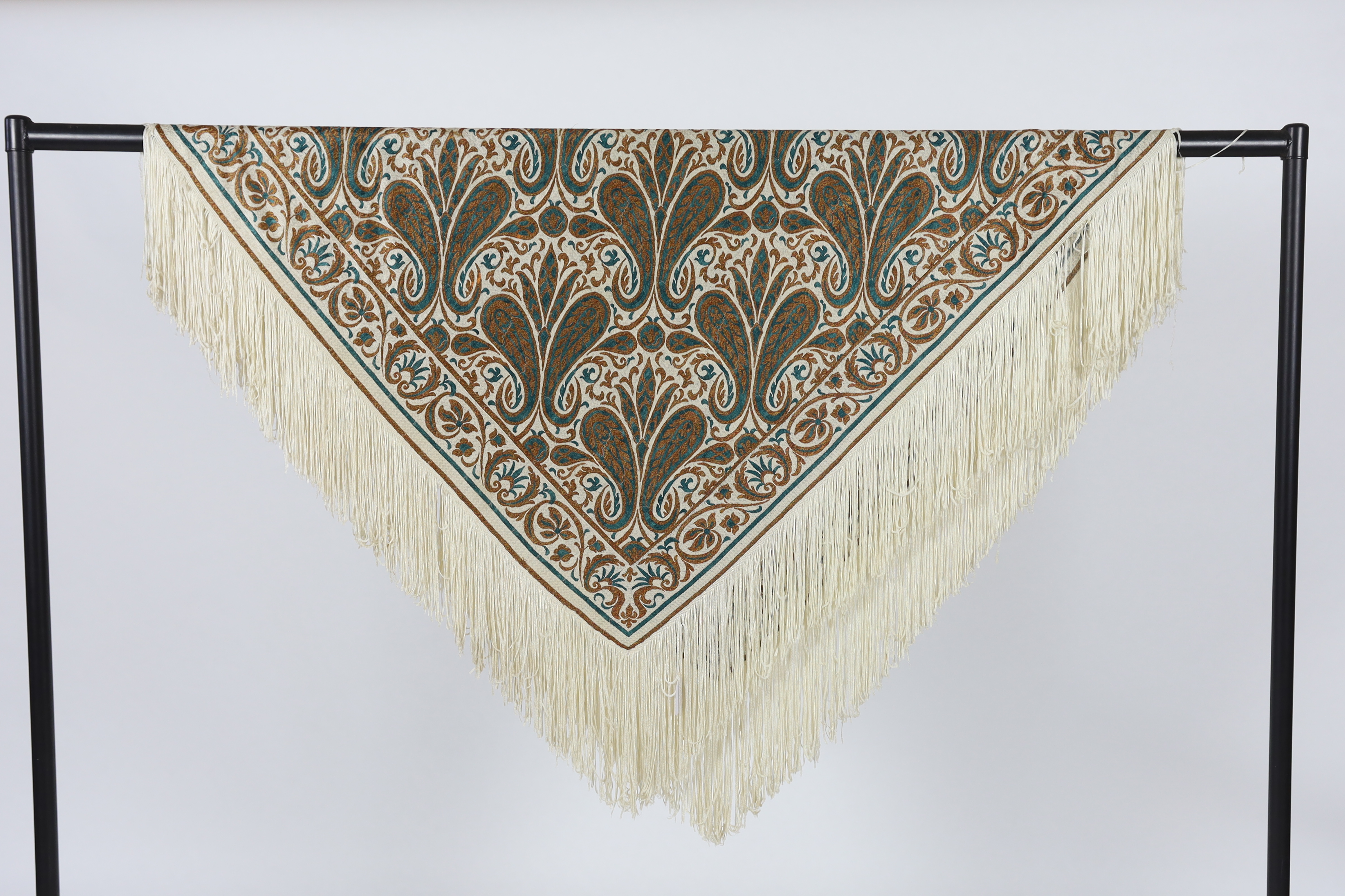 A 1920’s-1930’s cream silk woven shawl, woven with turquoise and bronze coloured silks in an all over tear drop paisley motif, edged with fine knitted cream fringing, approximately 109cm x 120cm